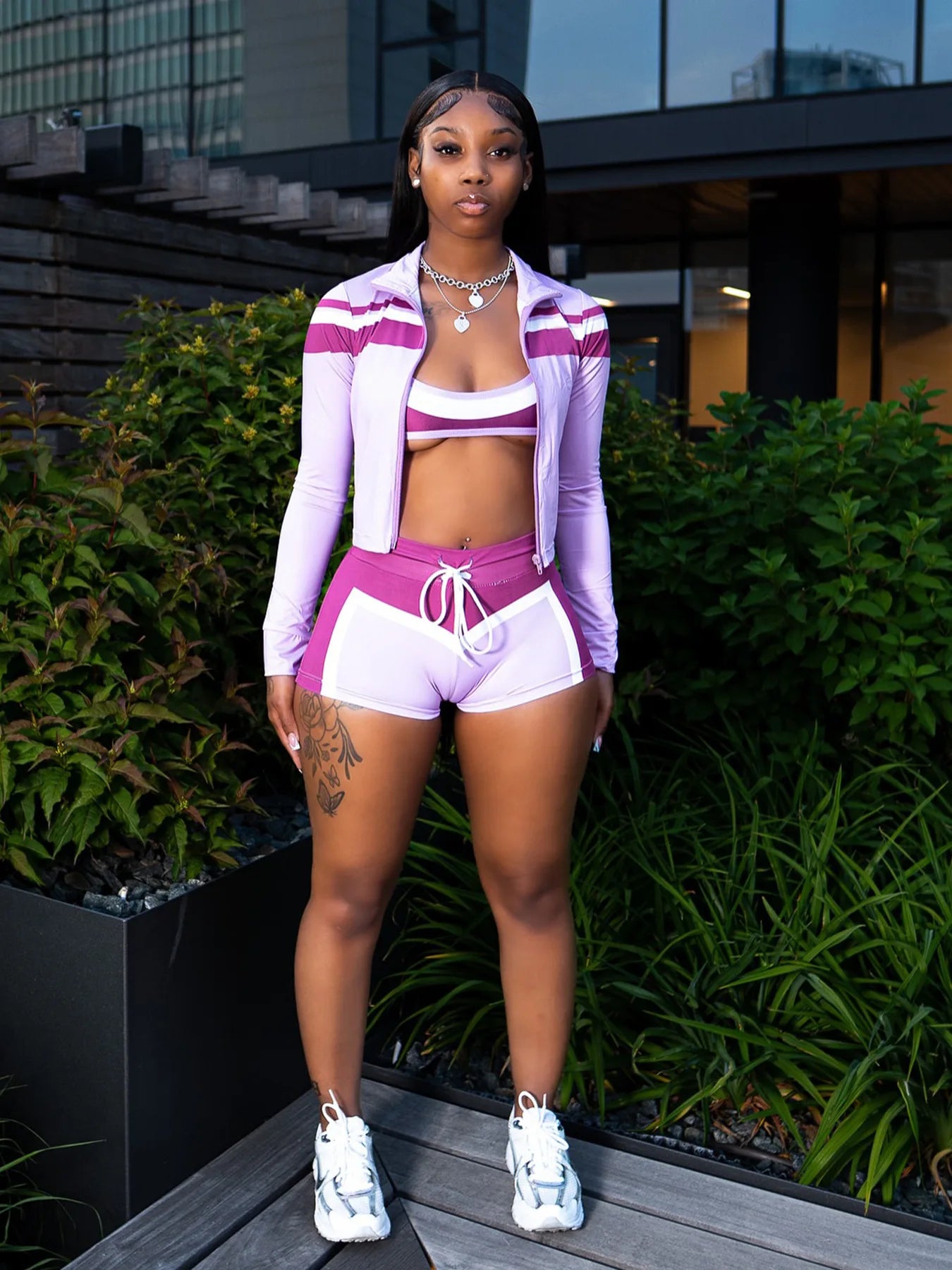 Woman in a purple athletic outfit standing outdoors with greenery in the background